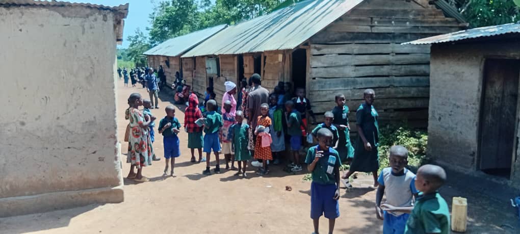 Children outside wooden classrooms at a school in Uganda